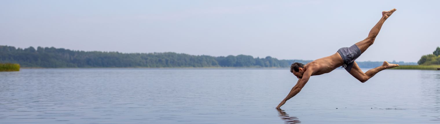 Ein Mann springt von einem Steg in den See.