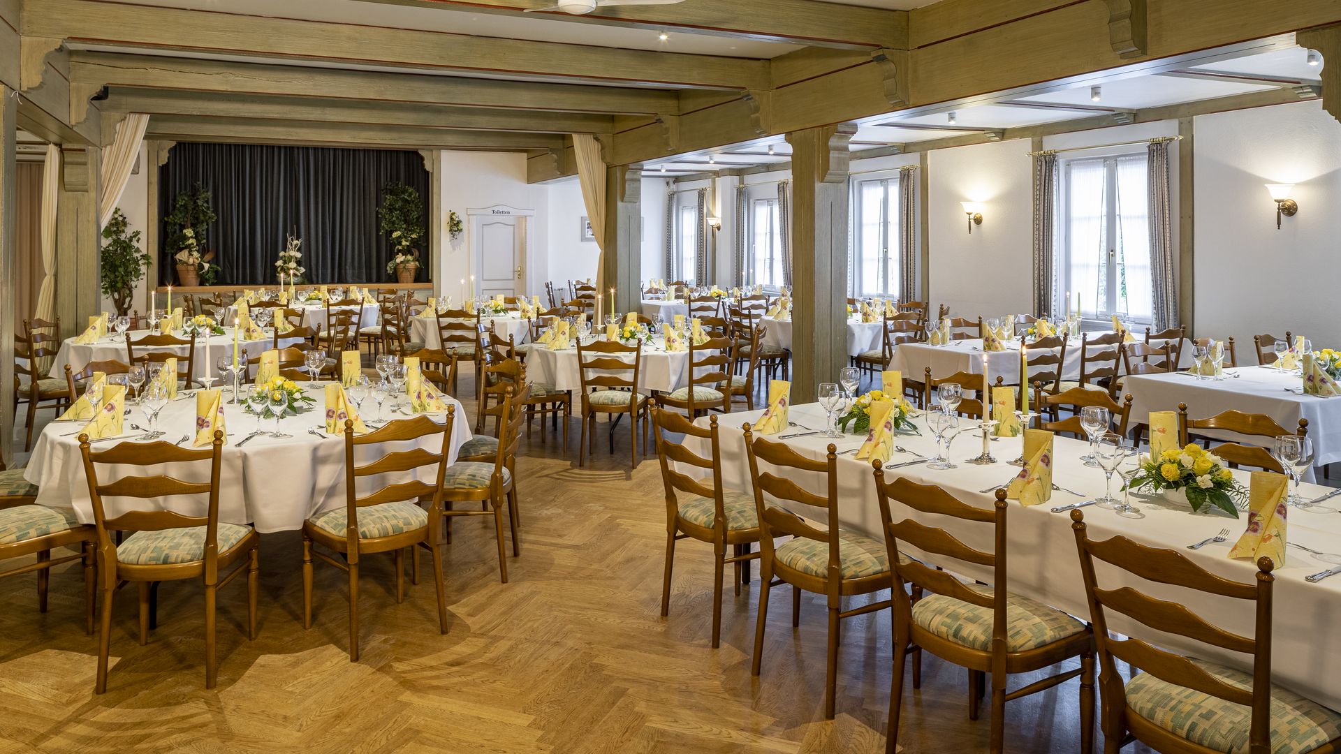 Großer Saal mit gedeckten Tischen und Bühne im Hintergrund