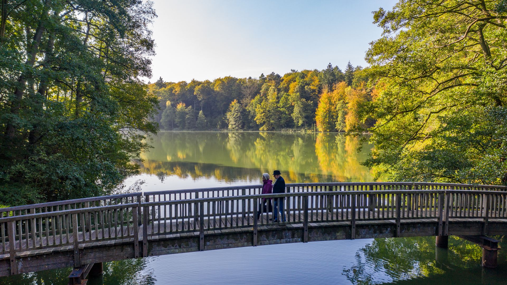 Spaziergänger laufen über Brücke am Schmalsee bei Mölln