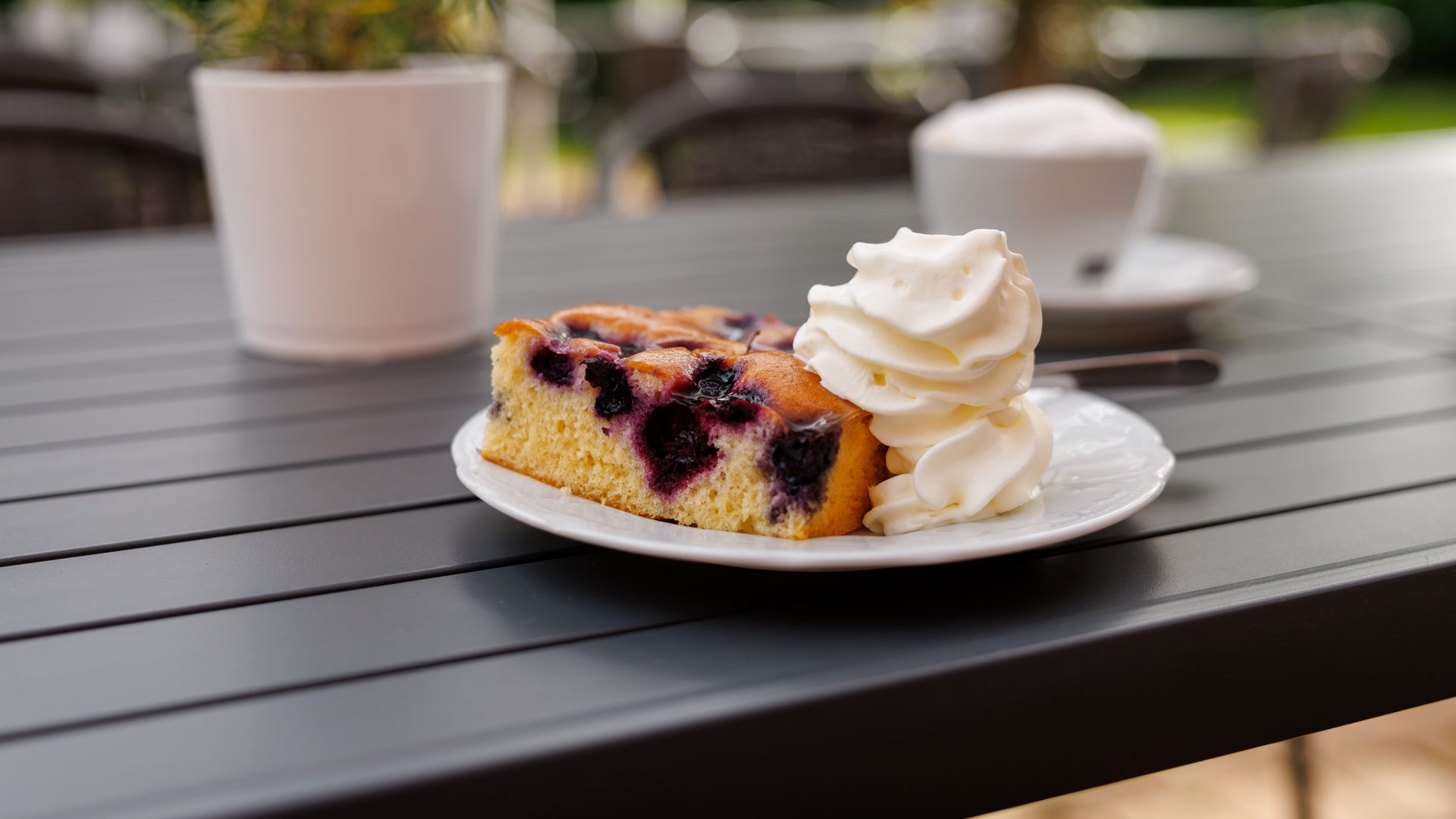 Café und Kuchen Patchwork Landhaus Köthel Teller mit Kuchen und Sahne, daneben eine Tasse Kaffee