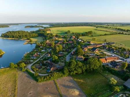 Village with many houses, green fields and water nearby, seen from above and in the sunshine.