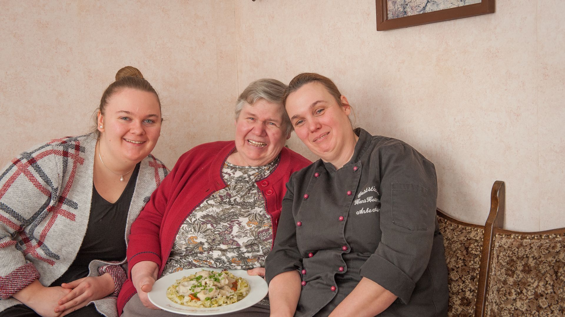 Drei Frauen mit einem Gericht mit Essen auf einer Bank.