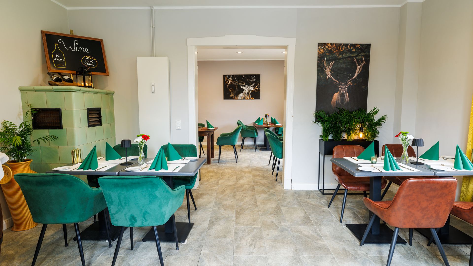 Bild mit gedeckten Tischen an denen Stühle stehen mit Kachelofen im Hintergrund.